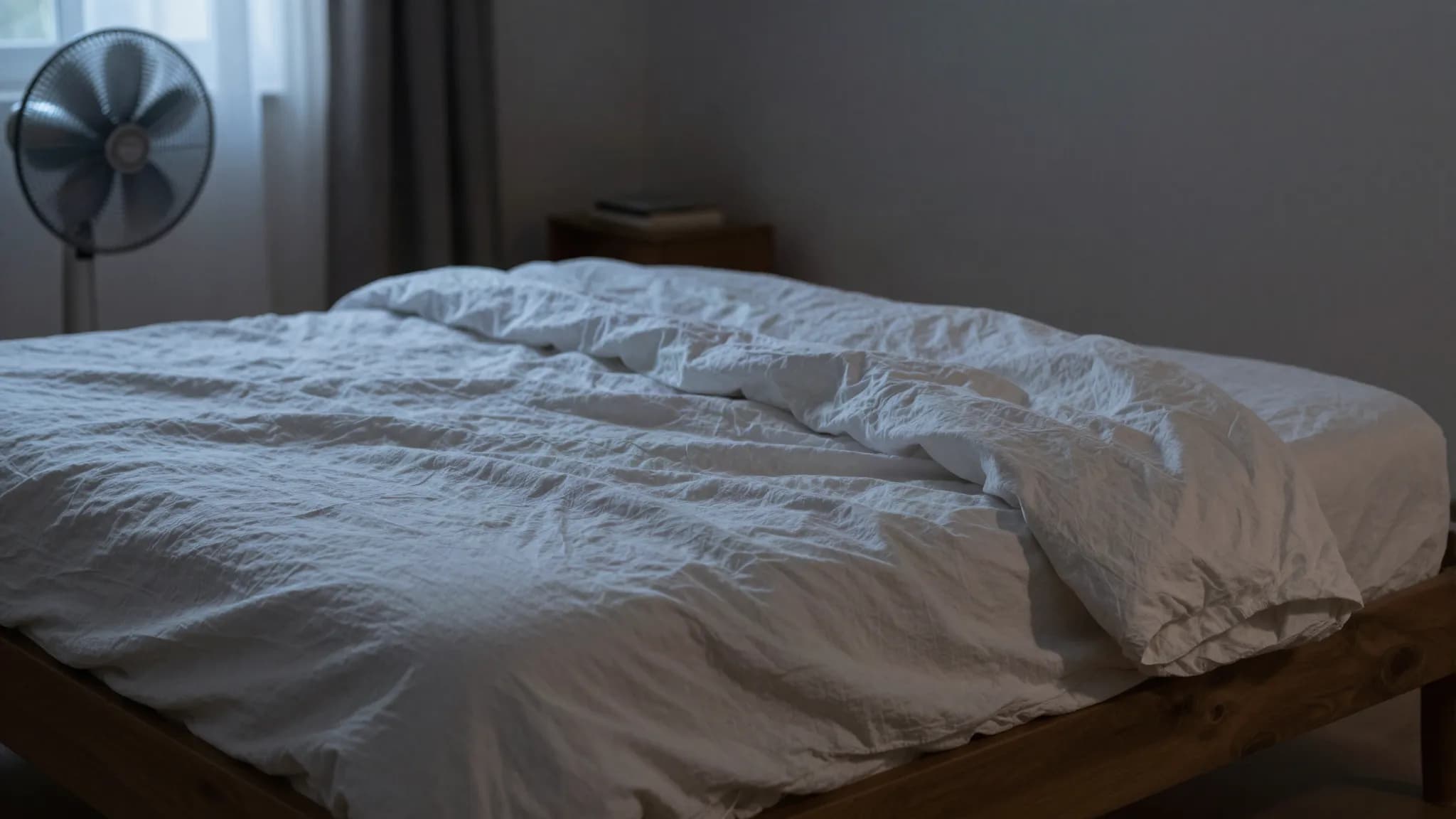 A bed made with light linen sheets in a dim bedroom at night