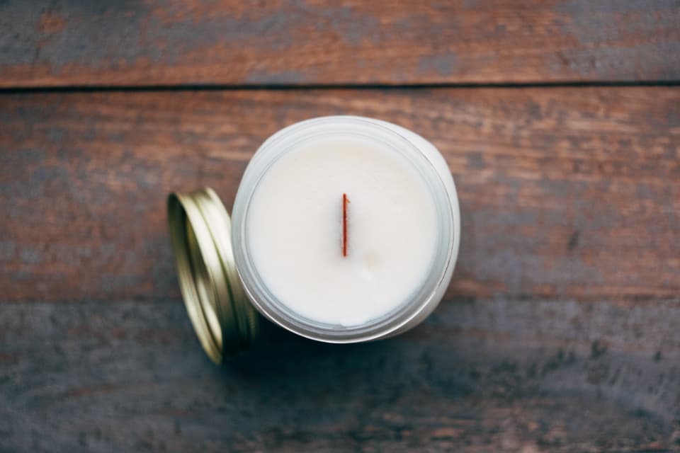 A white candle in a clean ceramic jar styled on a pale surface