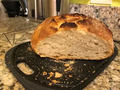 A crusty sourdough loaf cut open to reveal an open, airy crumb, next to a glass jar of bubbly active starter