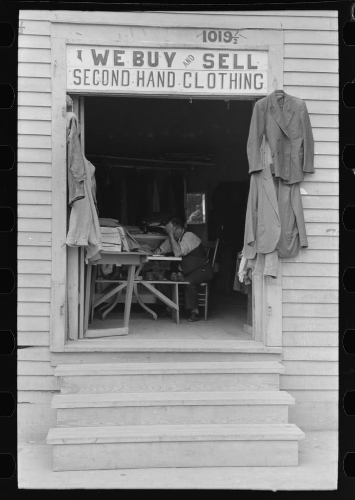 Organized racks of secondhand and vintage clothing in warm-lit boutique setting