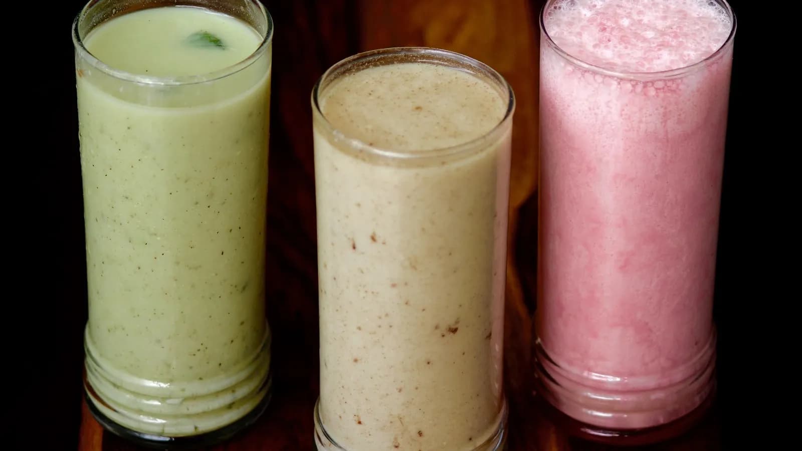 Three tall glasses of Indian dairy drinks side by side: mint chaas, cumin chaas and a pink rose lassi