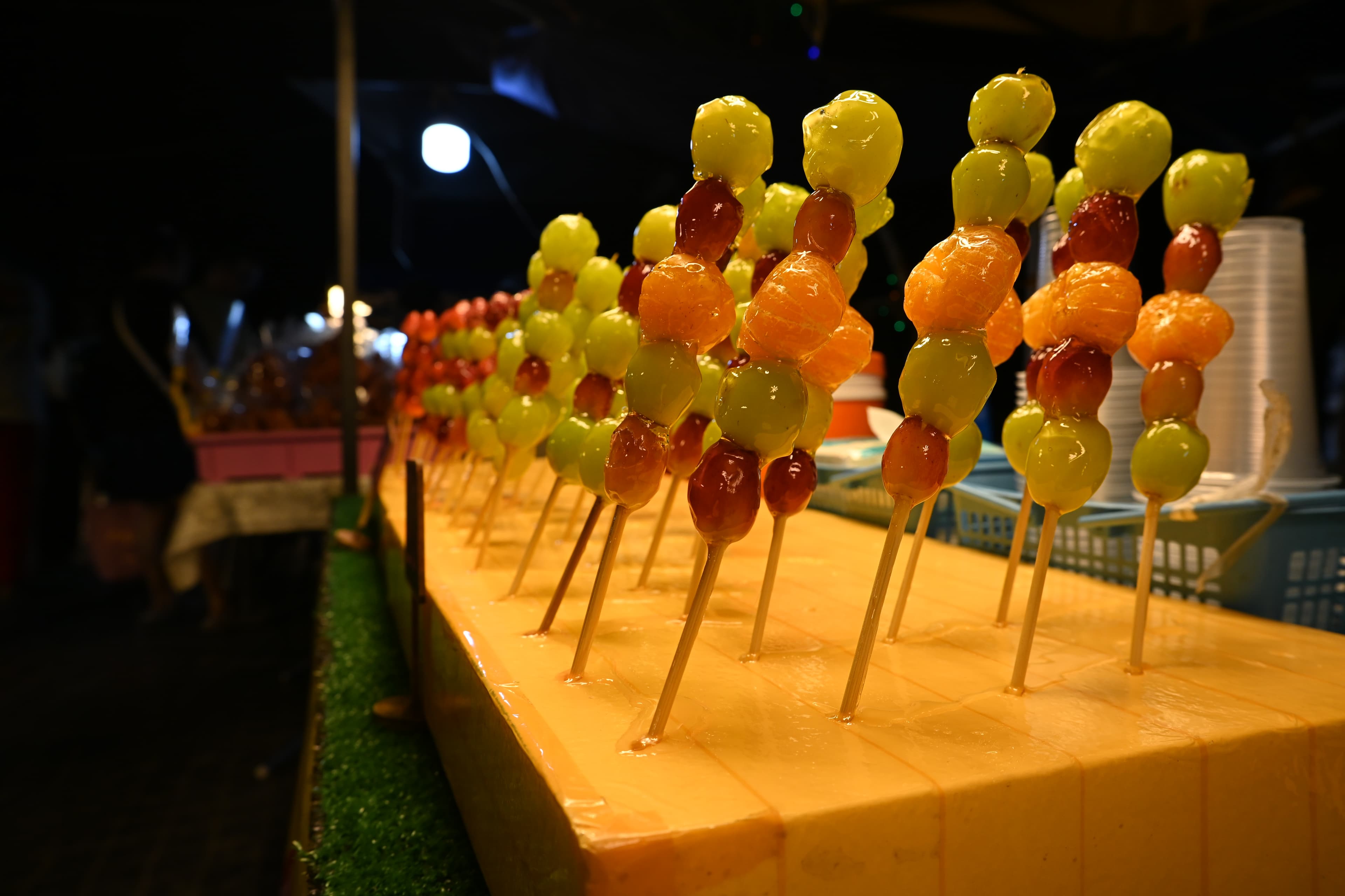 A row of glossy, sugar-glazed candied strawberry skewers with a hard, cracked candy shell, tanghulu style