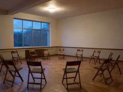 Editorial illustration of wooden folding chairs arranged in a circle in an empty community hall at dusk