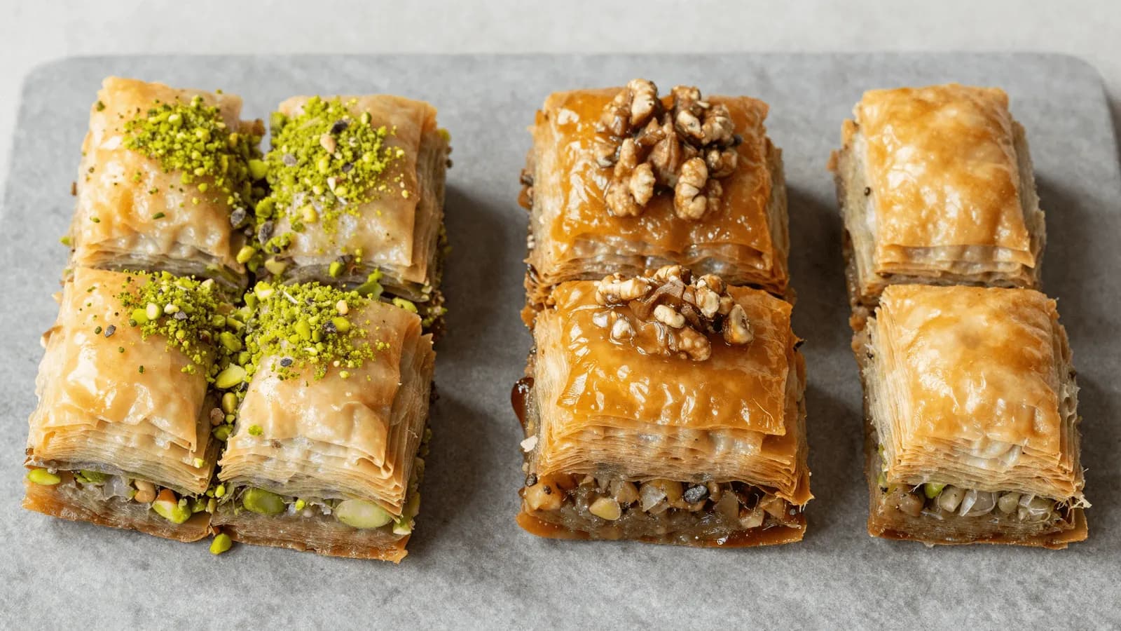 Two styles of baklava side by side, one topped with green pistachio and one darker with walnut