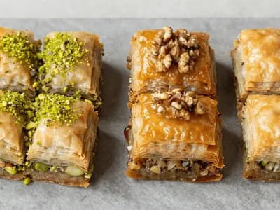 Two styles of baklava side by side, one topped with green pistachio and one darker with walnut