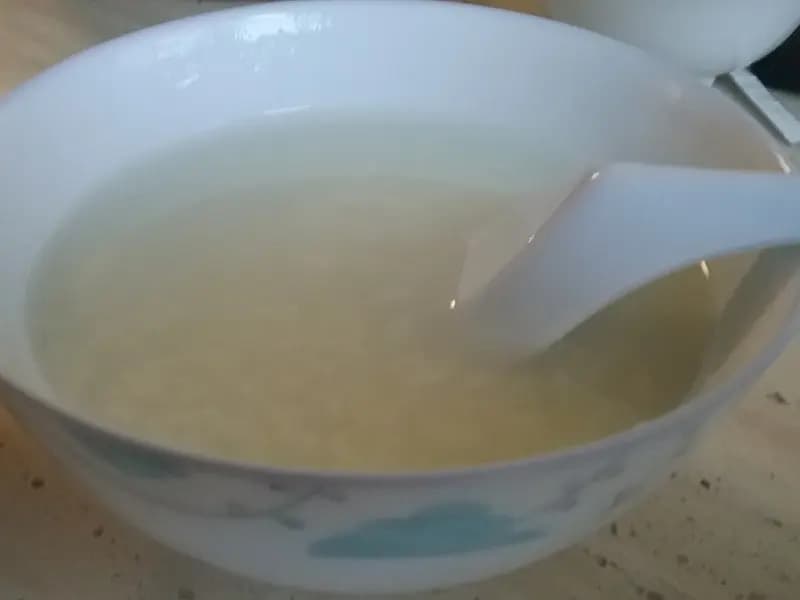 A bowl of plain white congee with a spoon resting in it, the rice grains cooked down until they have almost disappeared into the liquid