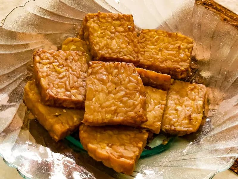 Slices of fried tempeh arranged on a plate, the individual soybeans still visible in the cake where the mould has bound them together