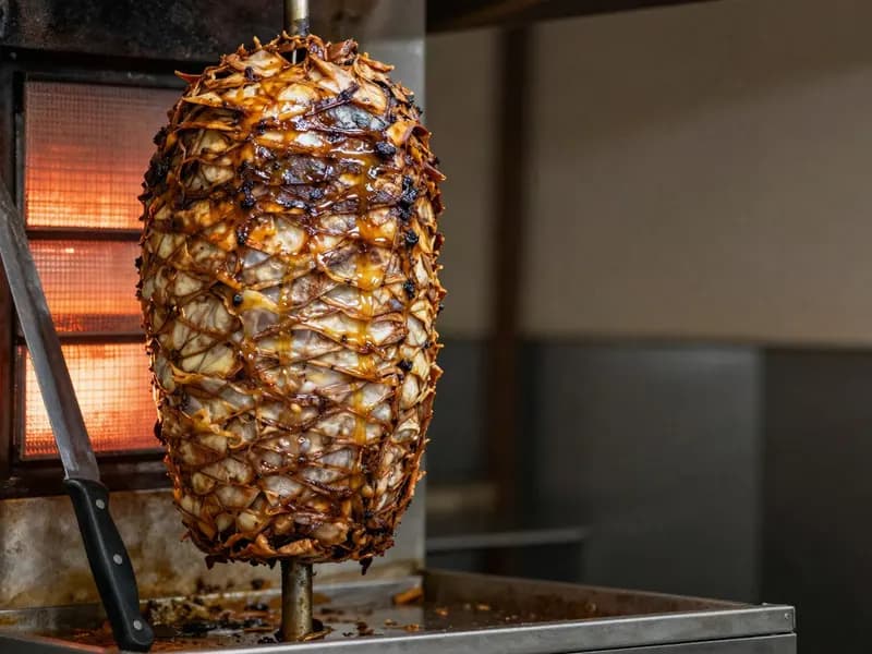 A vertical spit of layered shawarma meat turning in front of a heat source