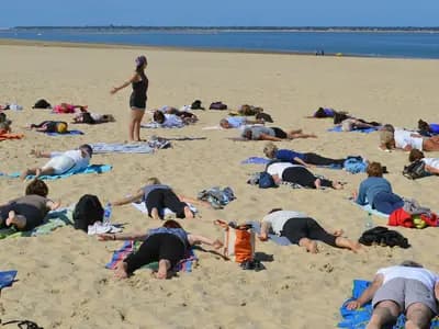 A large outdoor yoga class on a beach, participants spread across the sand following a teacher