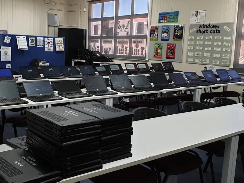 Rows of laptops on desks in an empty school computer room