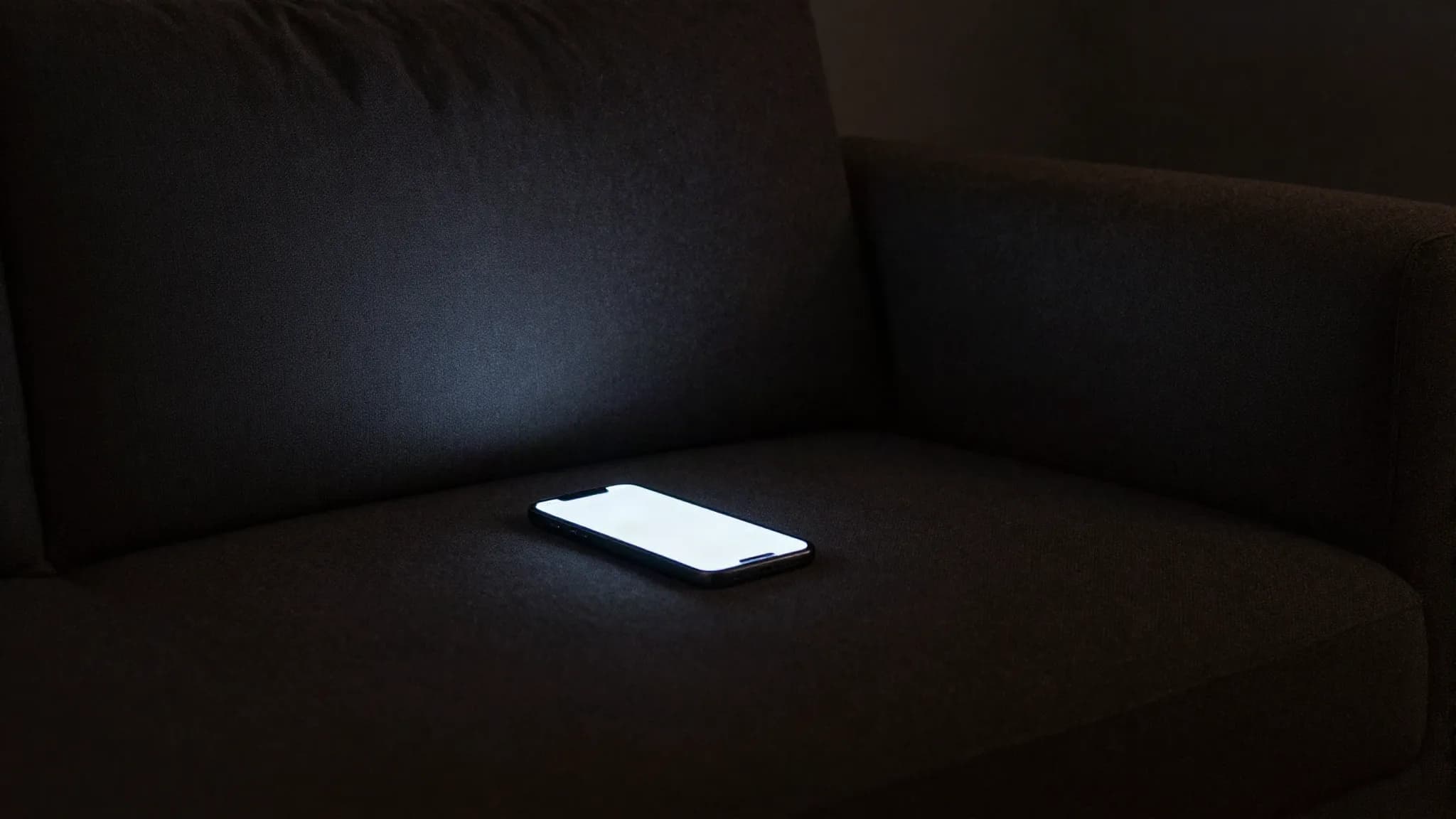 A phone glowing on an empty sofa in a dark room