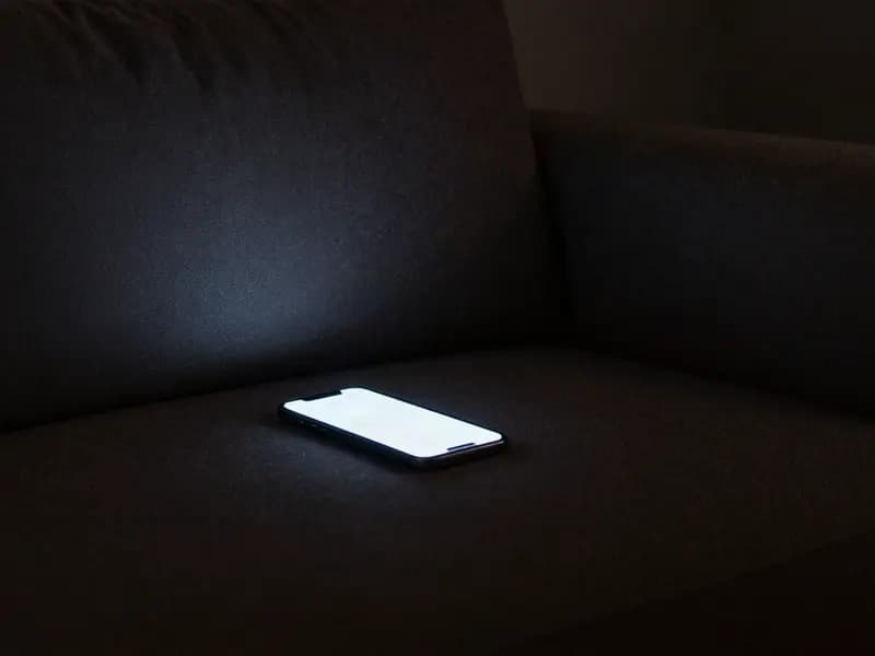 A phone glowing on an empty sofa in a dark room