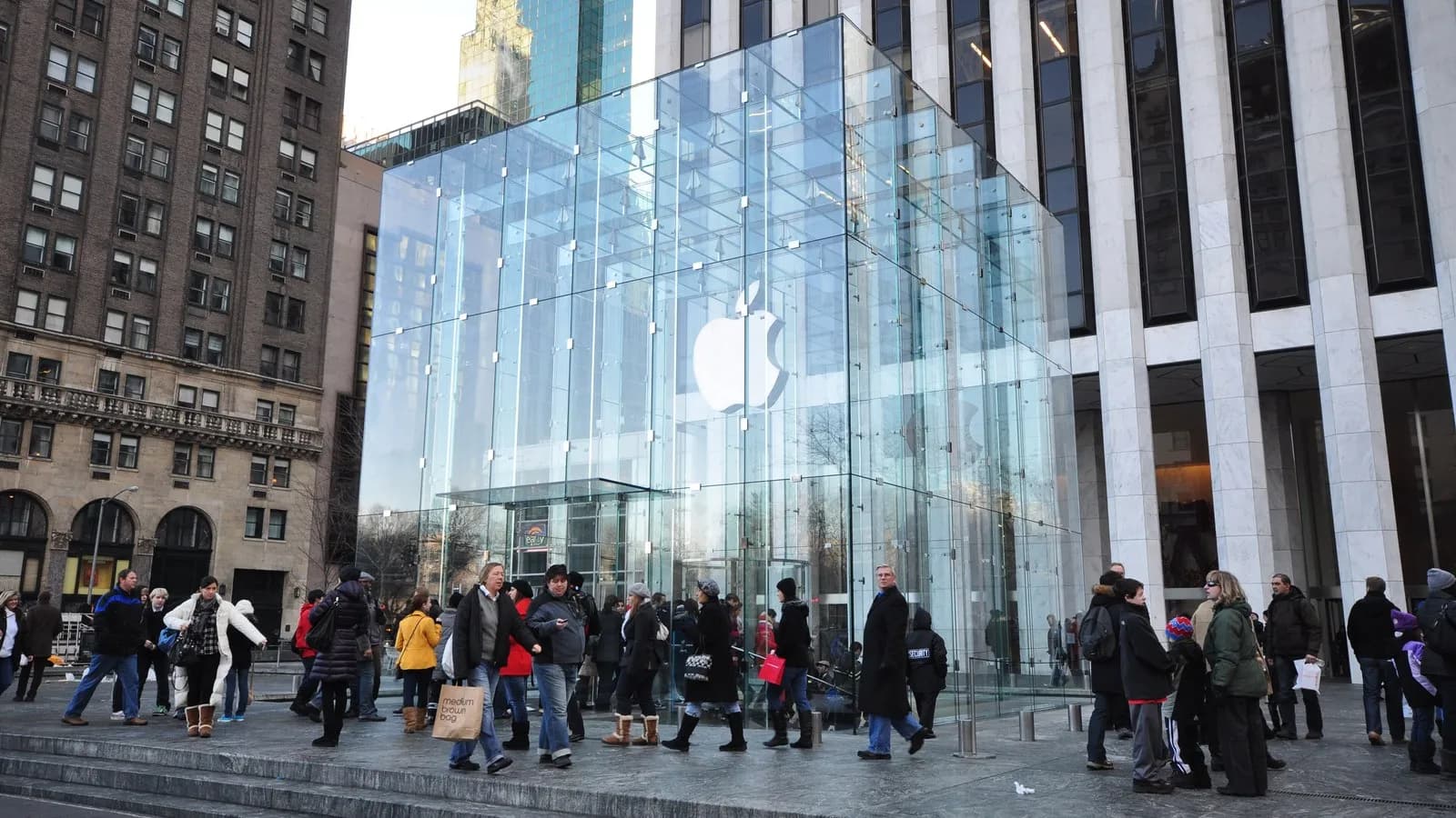 The glass cube of Apple's Fifth Avenue store in New York, with shoppers on the plaza in front of it