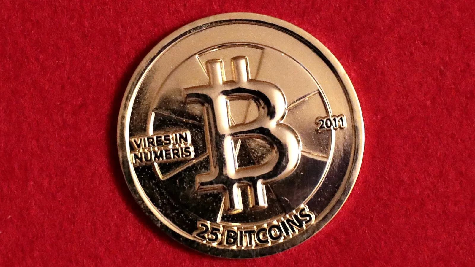 A gold-coloured 25 bitcoin Casascius physical coin stamped with a large B and the year 2011 lying on red cloth, photographed on 10 July 2019, an illustrative object photograph of bitcoin and not of Binance, its wallets or the funds involved