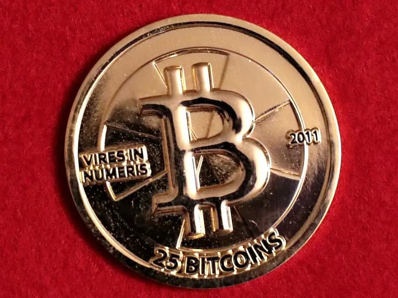 A gold-coloured 25 bitcoin Casascius physical coin stamped with a large B and the year 2011 lying on red cloth, photographed on 10 July 2019, an illustrative object photograph of bitcoin and not of Binance, its wallets or the funds involved