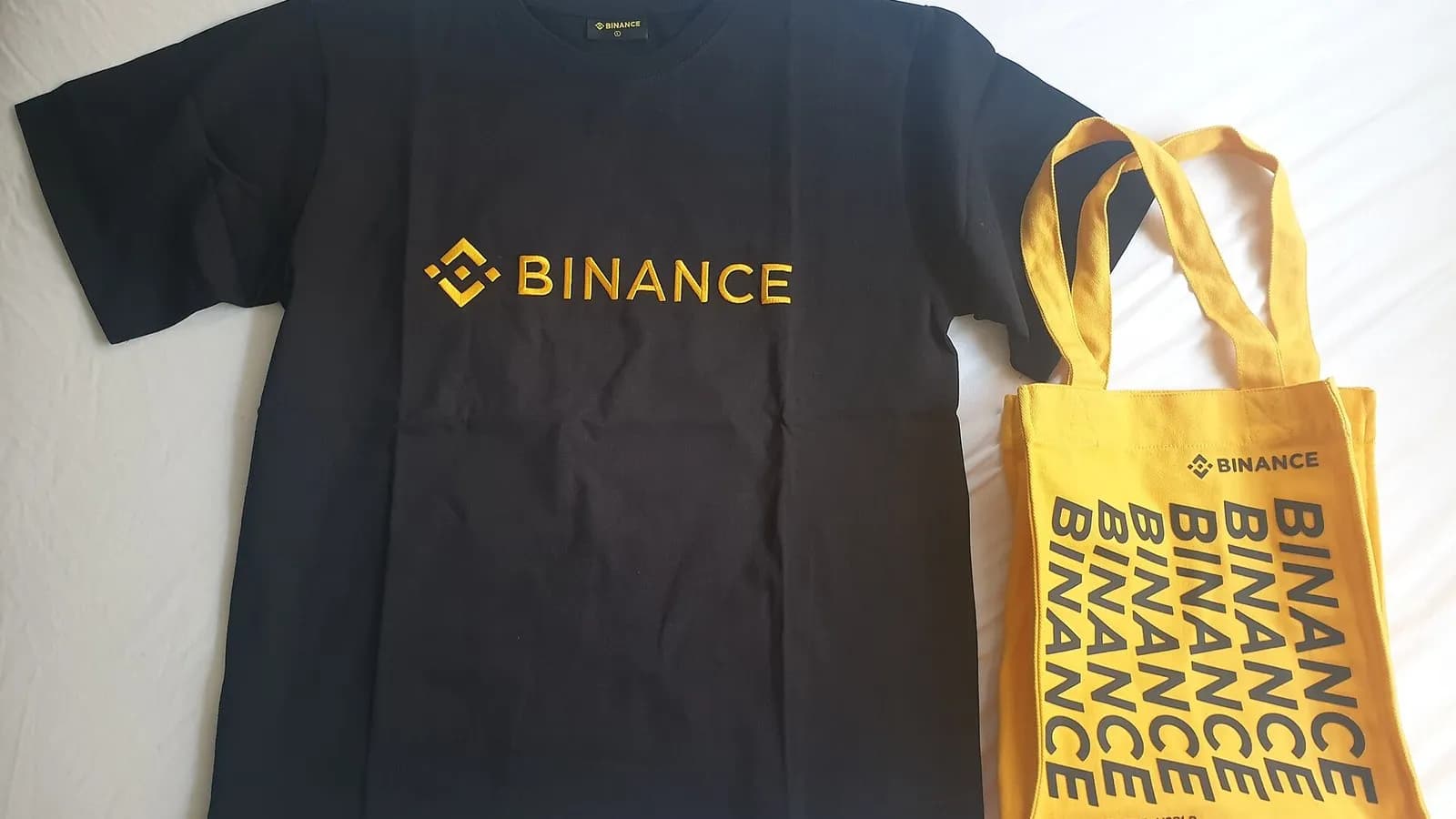 A black Binance T-shirt and a yellow Binance tote bag laid flat on a white surface, photographed on 9 July 2022, a file photograph of the exchange's own branded merchandise and not of the security incident