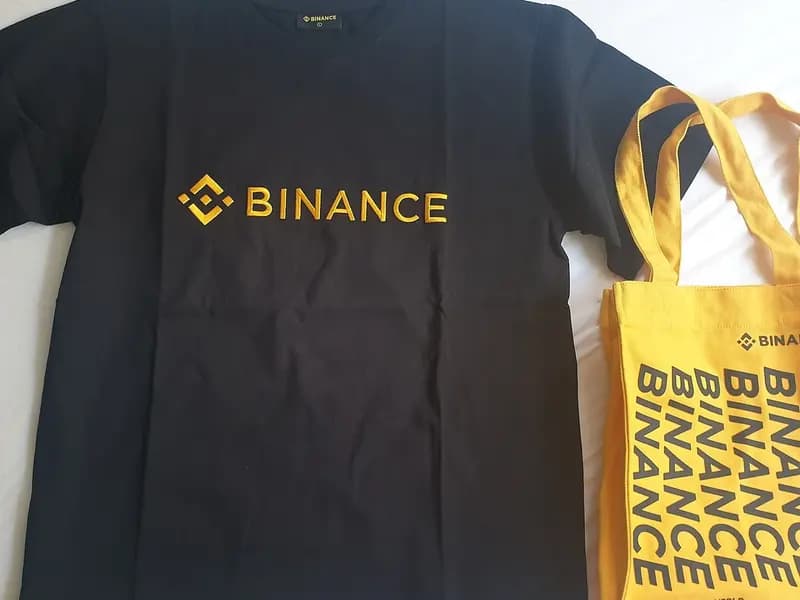 A black Binance T-shirt and a yellow Binance tote bag laid flat on a white surface, photographed on 9 July 2022, a file photograph of the exchange's own branded merchandise and not of the security incident