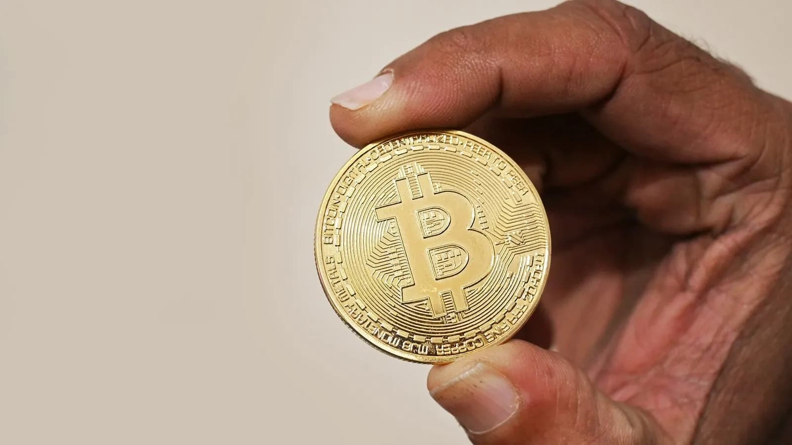 A hand holding up a gold-coloured physical bitcoin token against a plain beige background, photographed on 13 February 2023, a file photograph illustrative of bitcoin and not of this week's trading