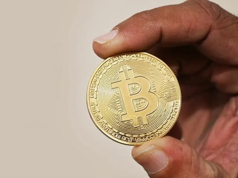 A hand holding up a gold-coloured physical bitcoin token against a plain beige background, photographed on 13 February 2023, a file photograph illustrative of bitcoin and not of this week's trading