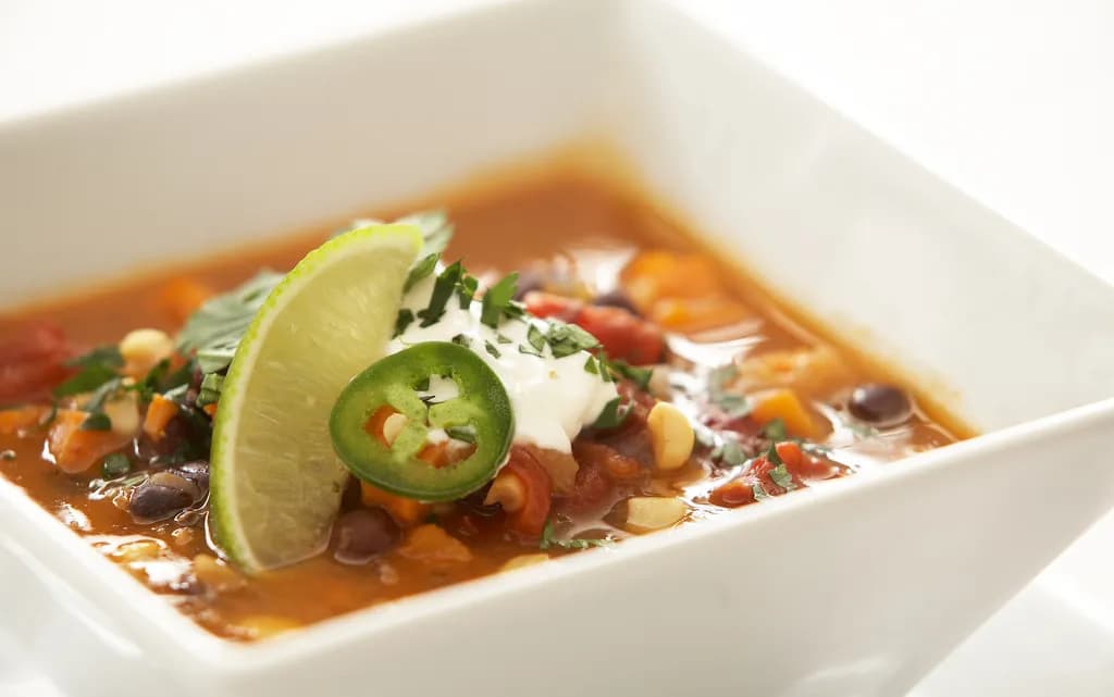 A steaming bowl of black bean sweet potato chili topped with sliced avocado, cilantro, and diced red onion