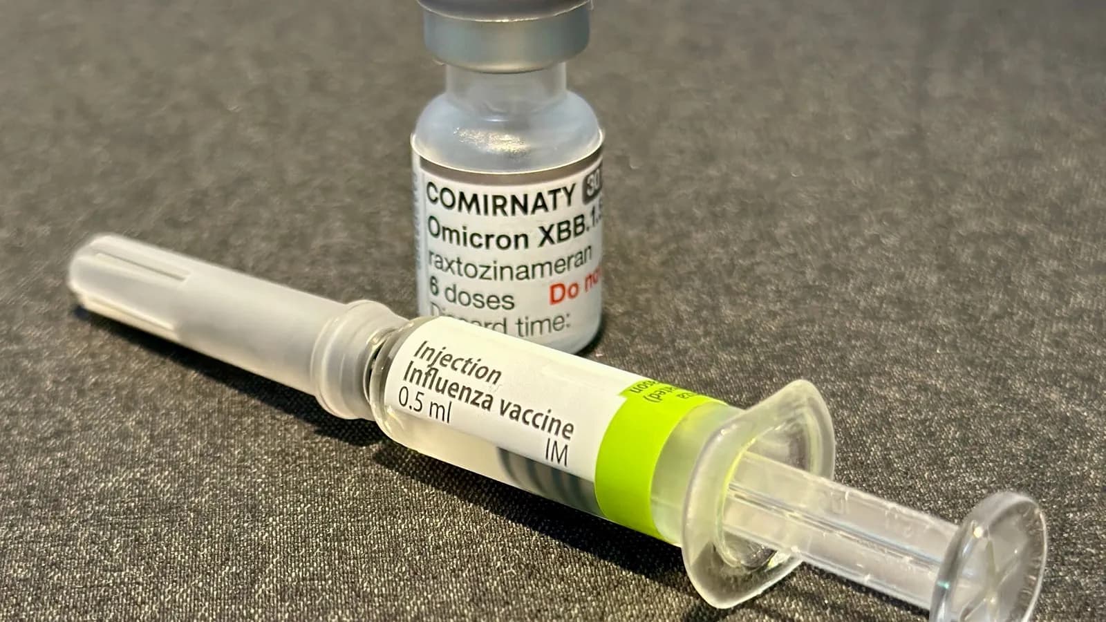 A COVID-19 vaccine vial alongside an influenza vaccine vial, illustrative of the kind of shots caught up in the CDC's stalled guidance process and not the specific mRNA flu vaccine named in this report, photographed in October 2023