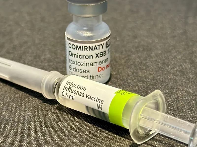 A COVID-19 vaccine vial alongside an influenza vaccine vial, illustrative of the kind of shots caught up in the CDC's stalled guidance process and not the specific mRNA flu vaccine named in this report, photographed in October 2023