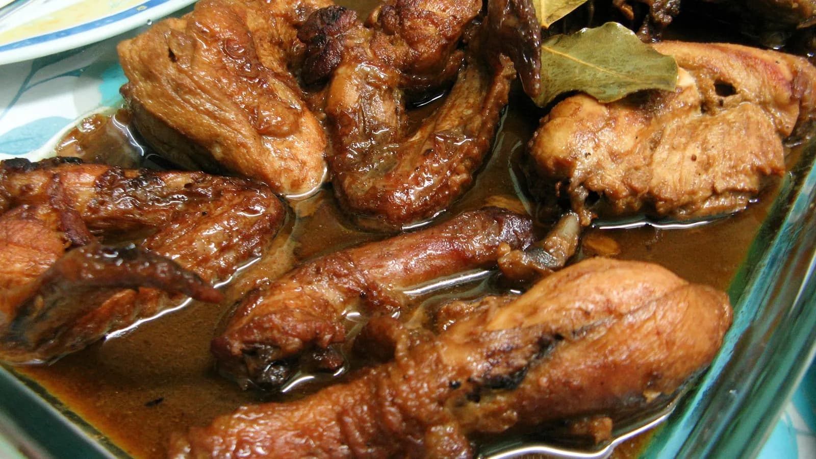 A glass dish of Filipino chicken adobo, drumsticks and thighs glossy in their reduced sauce with bay leaves, photographed in September 2009