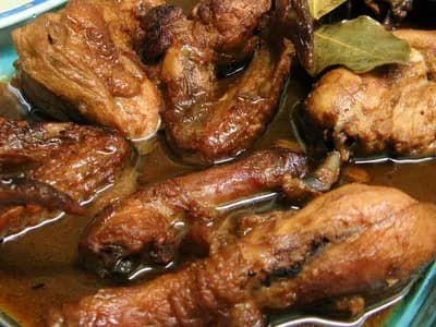 A glass dish of Filipino chicken adobo, drumsticks and thighs glossy in their reduced sauce with bay leaves, photographed in September 2009