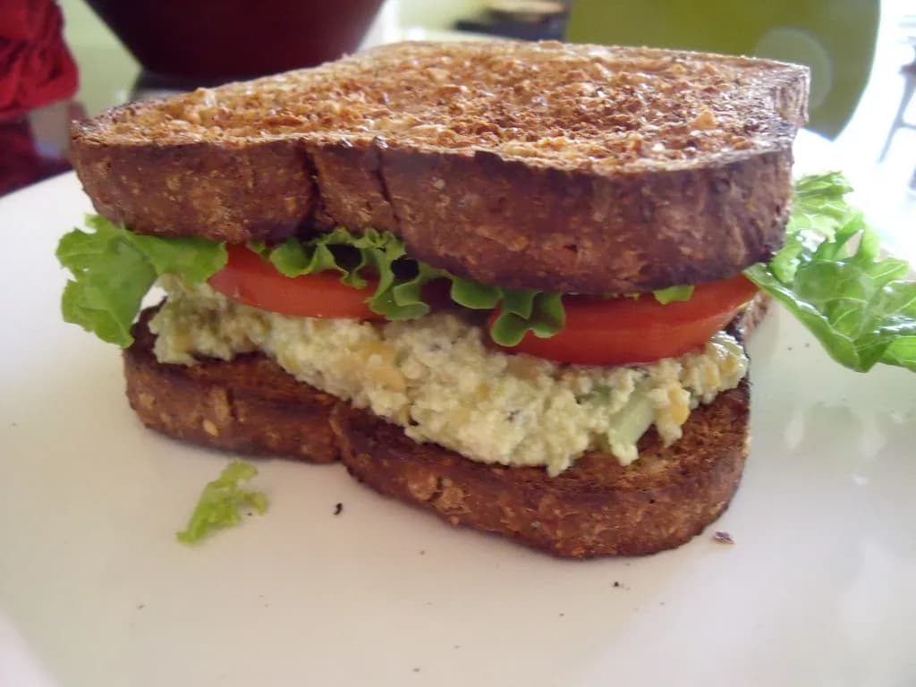 A generous scoop of chickpea salad on whole grain bread with dill and lemon garnish