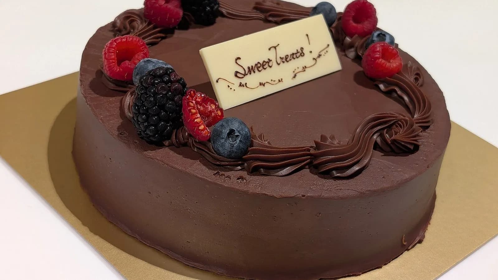 A whole round chocolate cake with glossy chocolate frosting piped around the edge and topped with raspberries and blueberries, photographed in Tokyo on 17 December 2024, a file photograph of a chocolate cake and not of this exact recipe