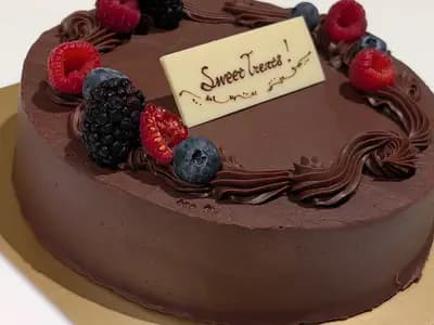 A whole round chocolate cake with glossy chocolate frosting piped around the edge and topped with raspberries and blueberries, photographed in Tokyo on 17 December 2024, a file photograph of a chocolate cake and not of this exact recipe