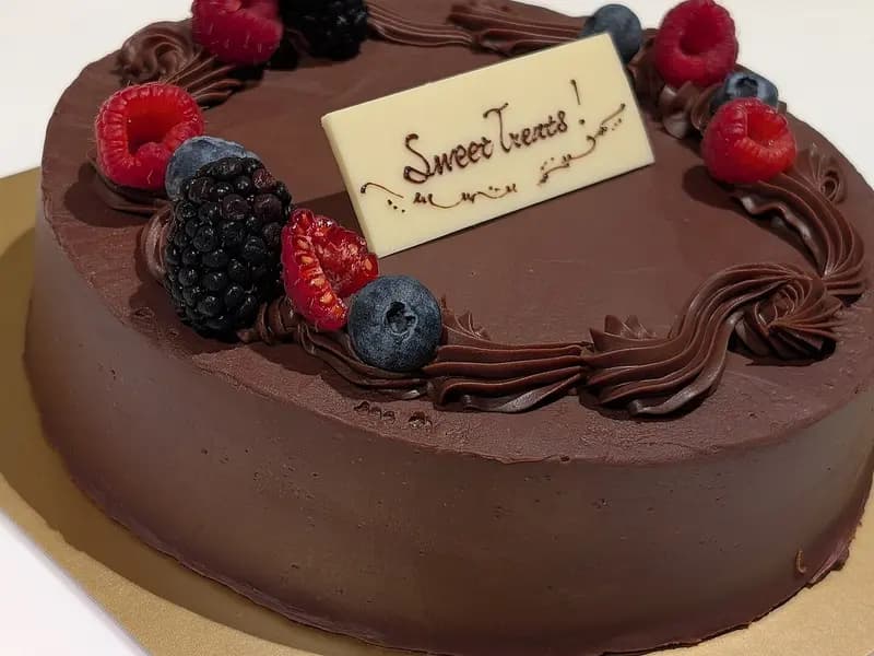 A whole round chocolate cake with glossy chocolate frosting piped around the edge and topped with raspberries and blueberries, photographed in Tokyo on 17 December 2024, a file photograph of a chocolate cake and not of this exact recipe
