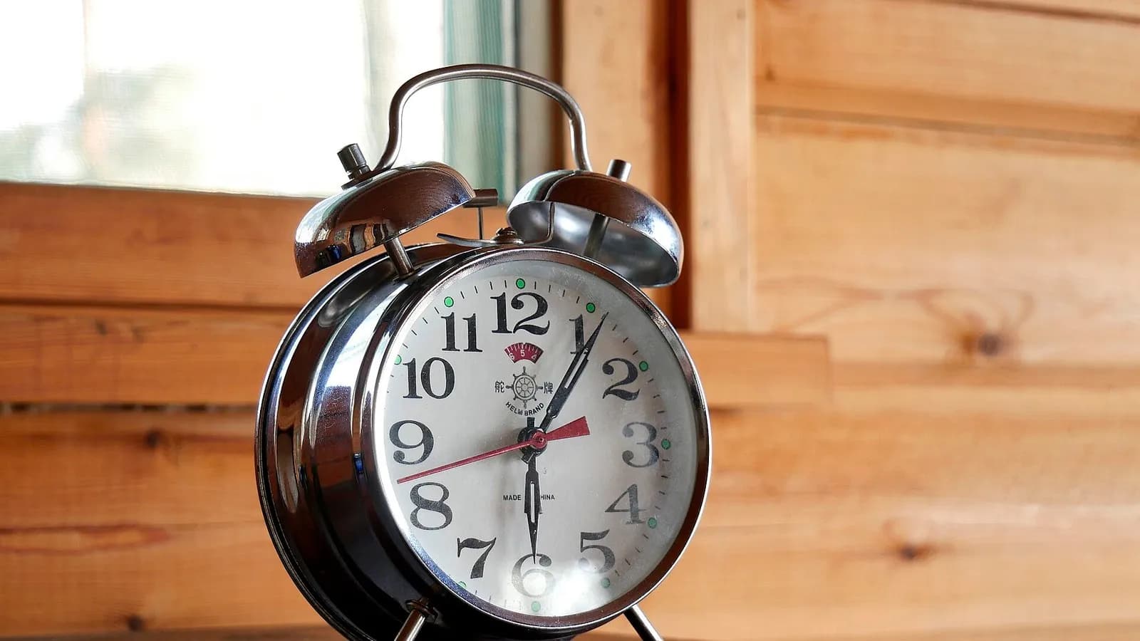 A chrome twin-bell alarm clock on a wooden shelf beside a window, photographed on 13 May 2018, a file photograph illustrative of sleep timing and not of any study participant