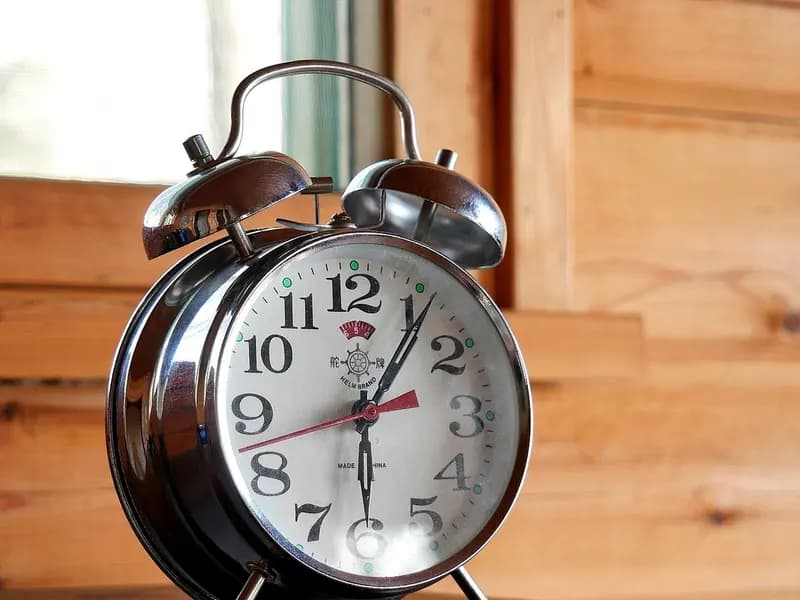 A chrome twin-bell alarm clock on a wooden shelf beside a window, photographed on 13 May 2018, a file photograph illustrative of sleep timing and not of any study participant