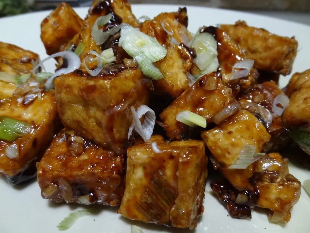 Golden-brown crispy tofu cubes glistening with peanut sauce, served over rice with cucumber slices