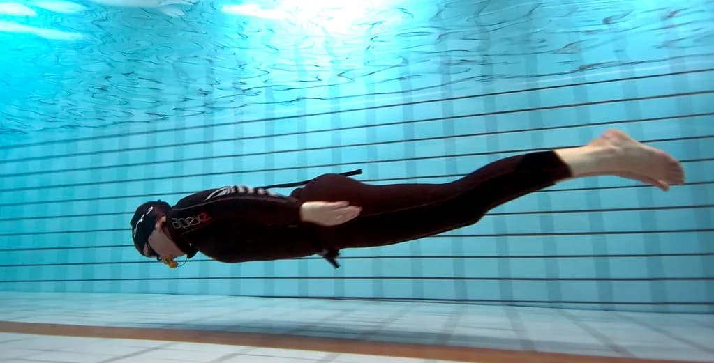Divers descending through clear water in a deep indoor pool