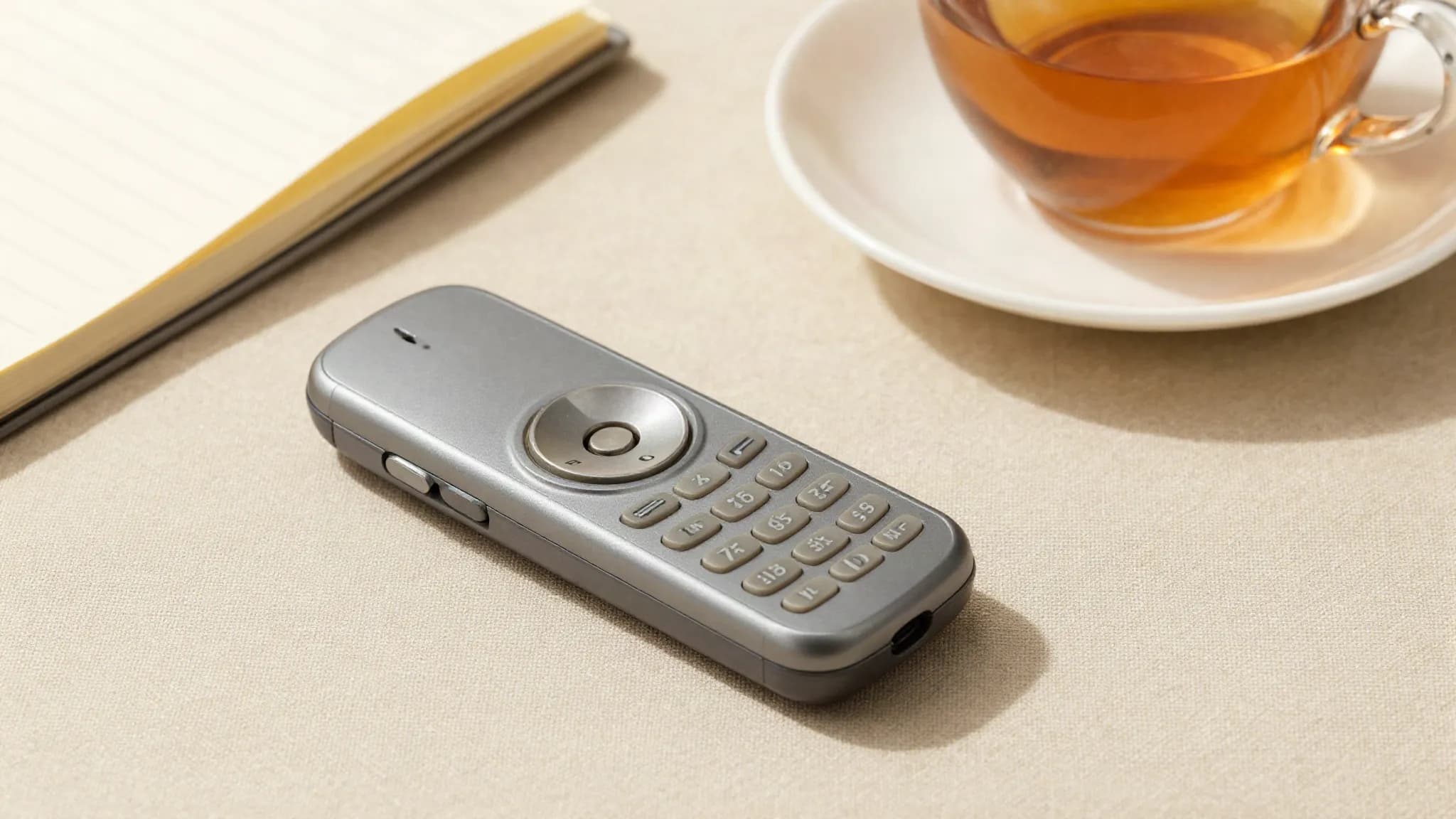 A basic feature phone beside a notebook and tea