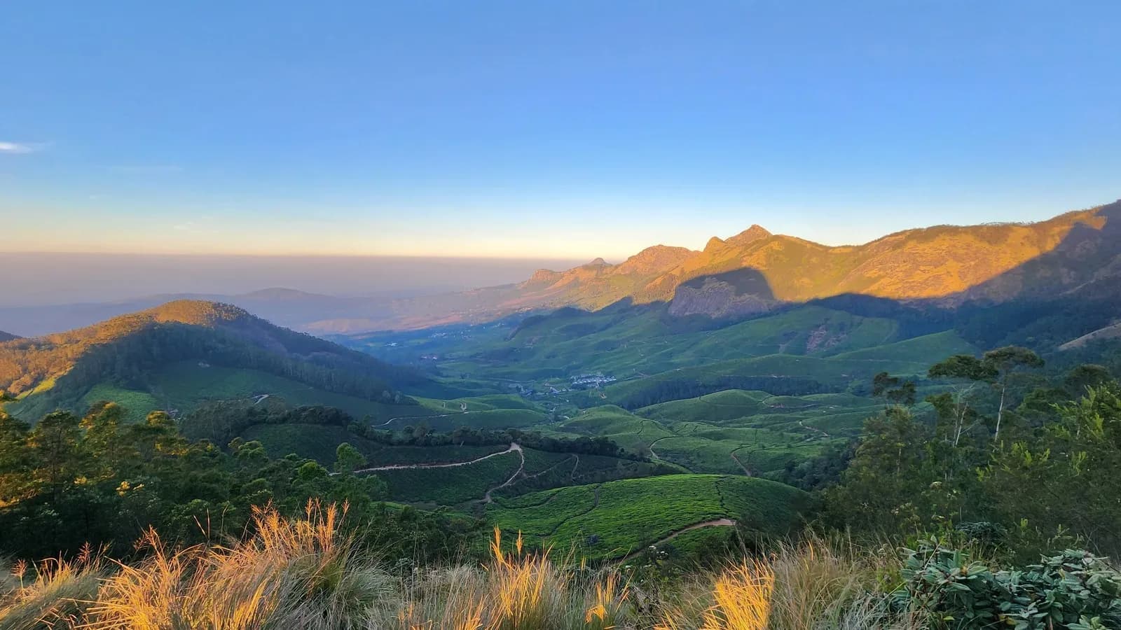 Sunrise over tea plantations and layered mountain ridges at Munnar in Kerala, the low early light that the Ayurvedic daily routine is built around