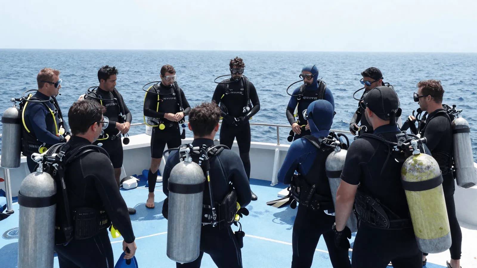 A group of divers gathered around an instructor for a pre-dive briefing on a boat deck