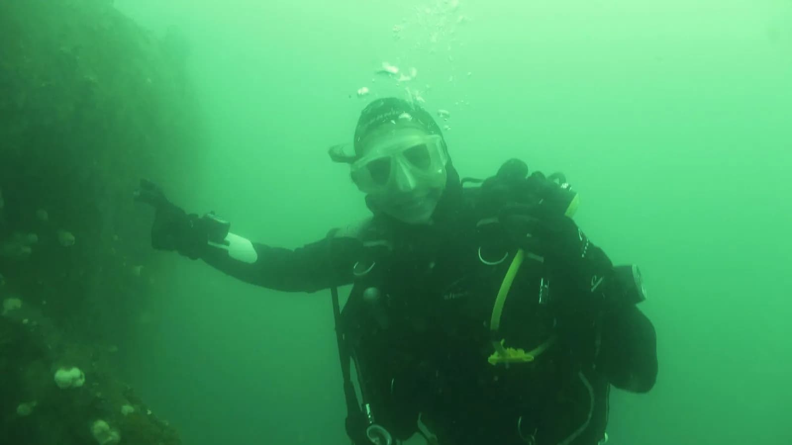 A diver holding a torch in green low visibility water on a wreck, the beam scattering off particles in front of them