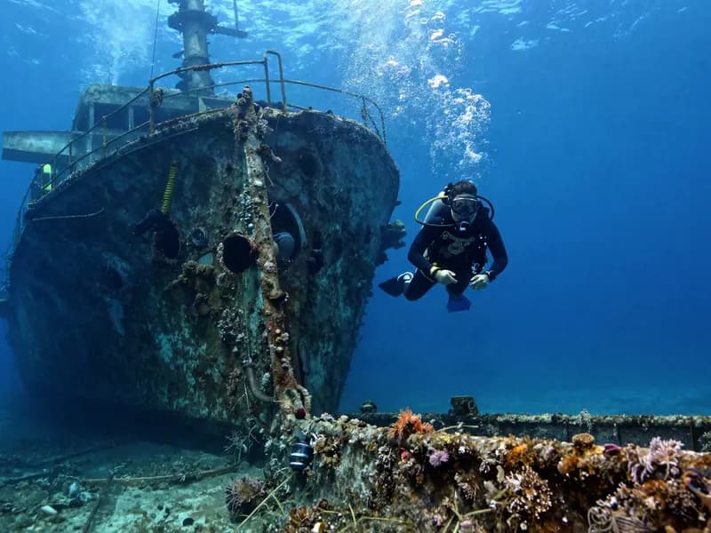 A diver approaching a sunken shipwreck in blue water