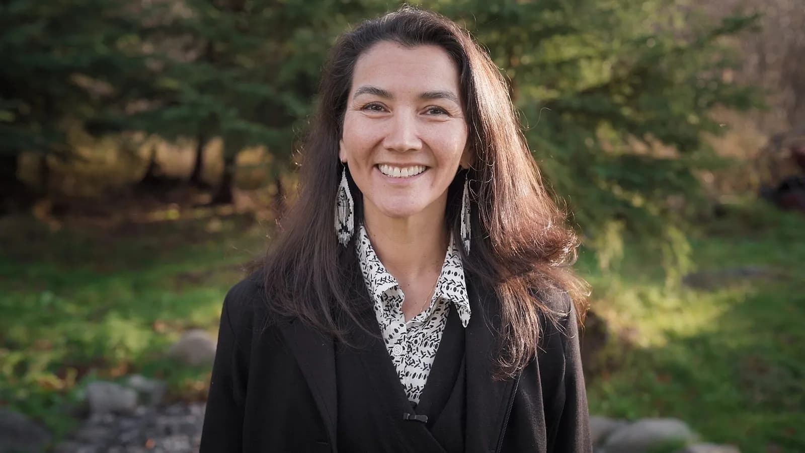 Mary Peltola, the Democratic Senate candidate in Alaska, smiling in a dark jacket and patterned blouse with long dark hair and drop earrings against a blurred green woodland, photographed in 2022, a file portrait of Peltola and not of the lawsuit or any court proceeding