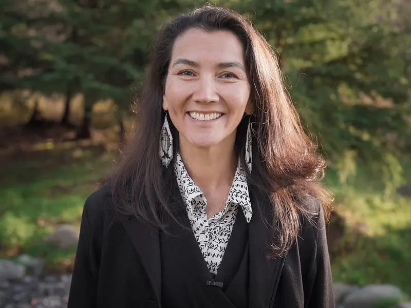 Mary Peltola, the Democratic Senate candidate in Alaska, smiling in a dark jacket and patterned blouse with long dark hair and drop earrings against a blurred green woodland, photographed in 2022, a file portrait of Peltola and not of the lawsuit or any court proceeding