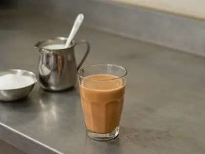 A glass of karak chai beside condensed milk and sugar