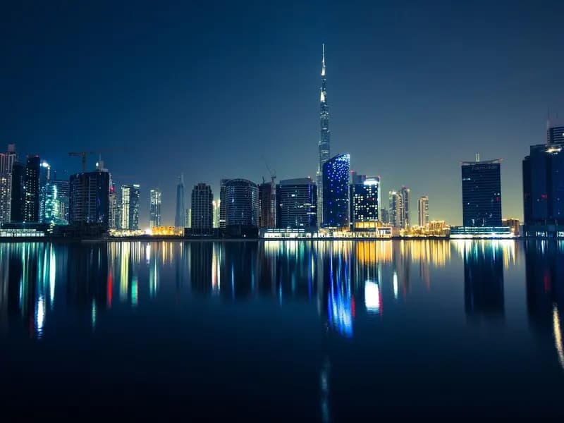 The Dubai skyline at night, with the Burj Khalifa at its centre and the towers of Business Bay reflected in the water