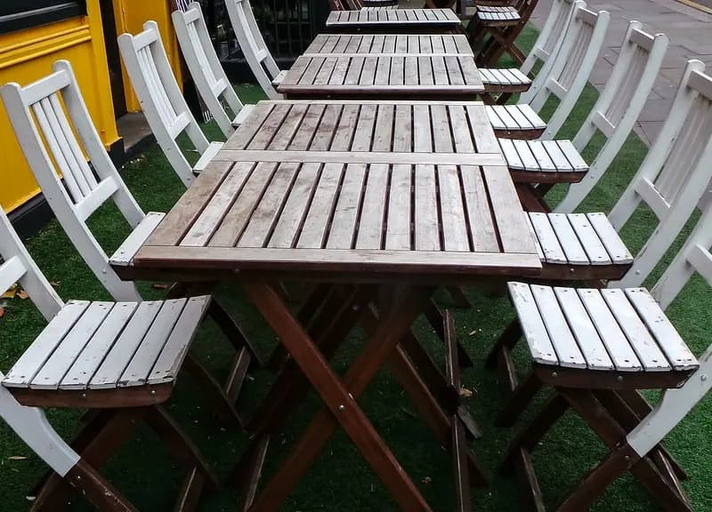 Empty wooden tables and chairs set out on the pavement outside a cafe