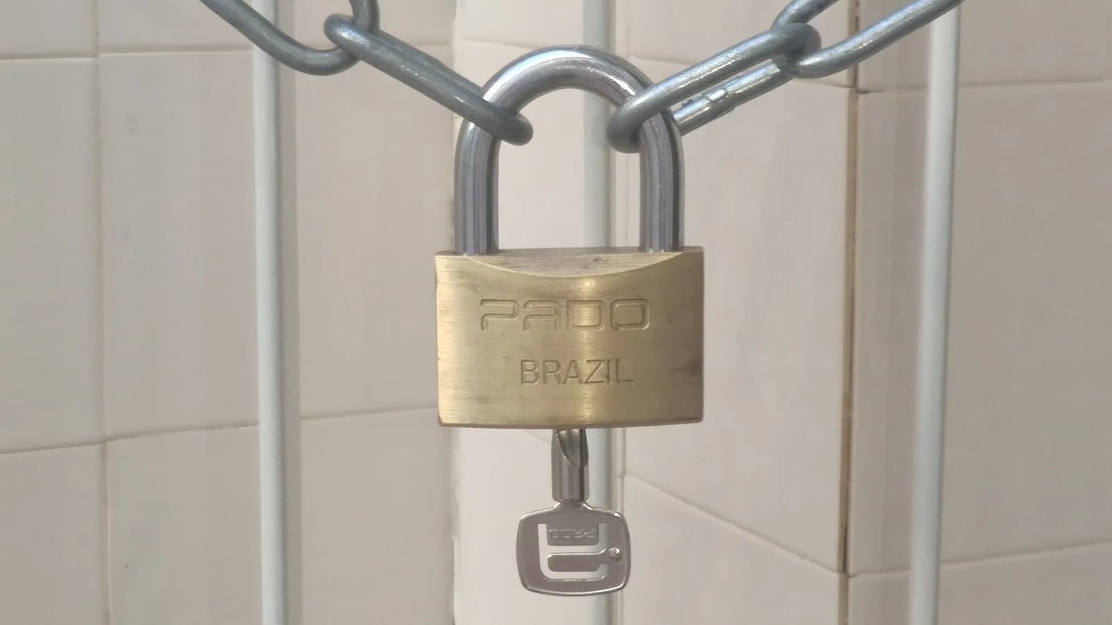 A brass padlock hanging on a steel chain against a tiled wall with its key below, photographed on 9 February 2023, a file photograph illustrative of security and not of eMudhra or its certificates