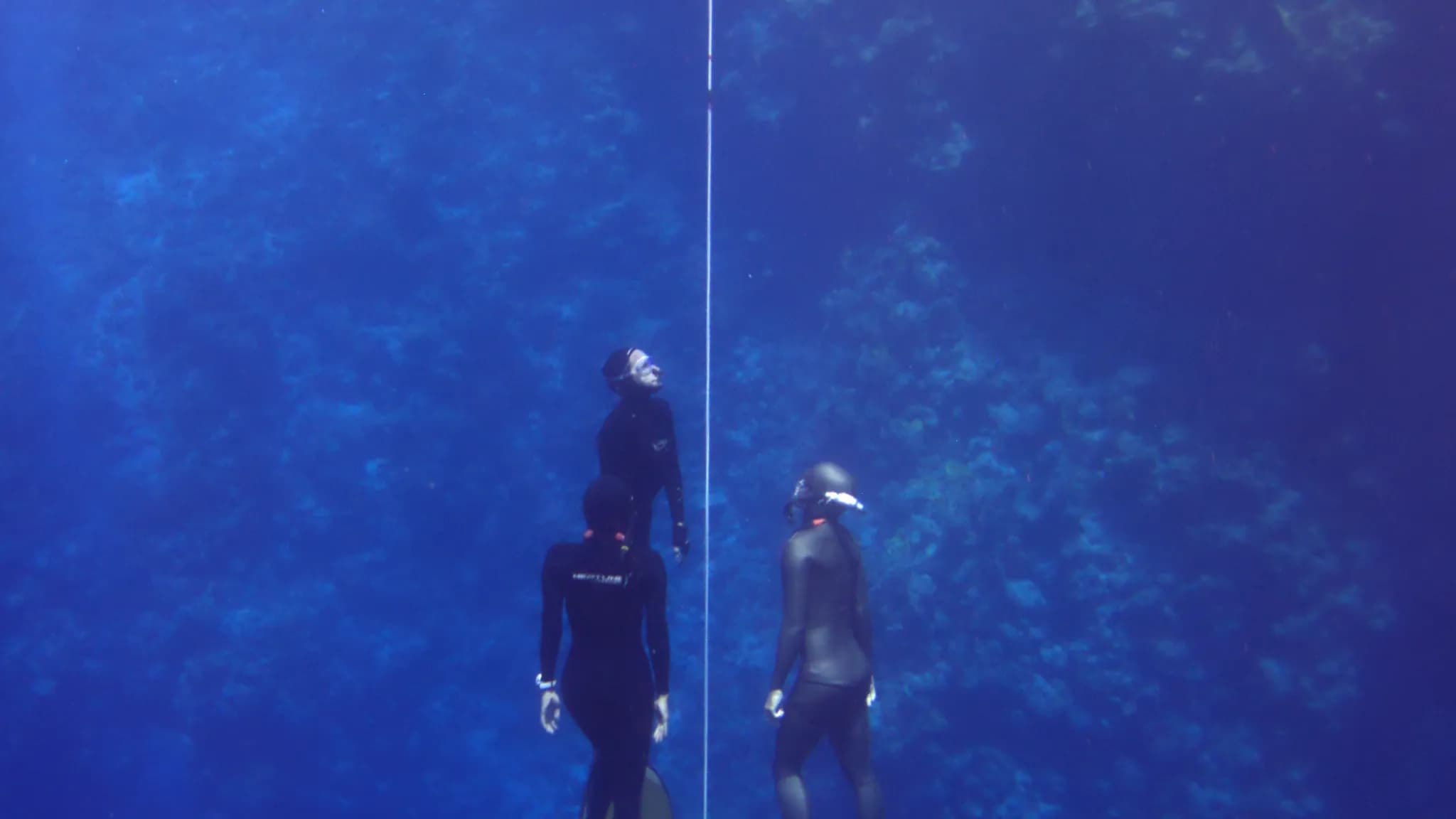 A freediver descending a vertical line into deep blue open water