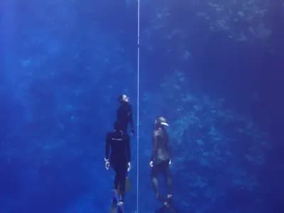 A freediver descending a vertical line into deep blue open water