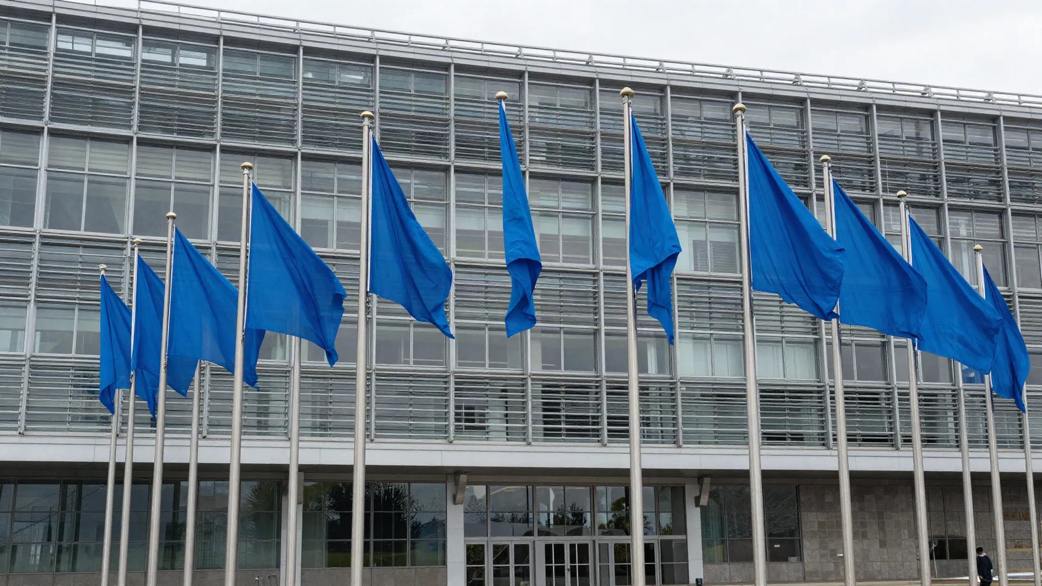 A modern institutional building with plain blue flags